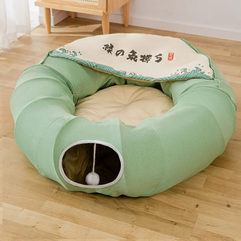 Una cama para mascotas diseñada para gatos. Tiene forma circular con un borde elevado, lo que proporciona un espacio acogedor y cerrado para que descanse el gato. La cama está cubierta con una tela que tiene un estampado y algunos caracteres japoneses.