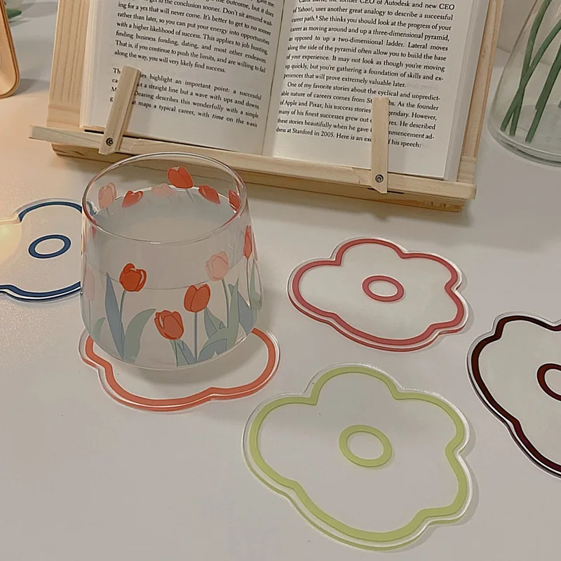 Un libro con un marcapáginas insertado, un vaso con diseño floral y varias pegatinas decorativas o calcas con motivos florales. El libro parece estar abierto en una página con texto, pero el contenido del texto no es visible en la imagen.