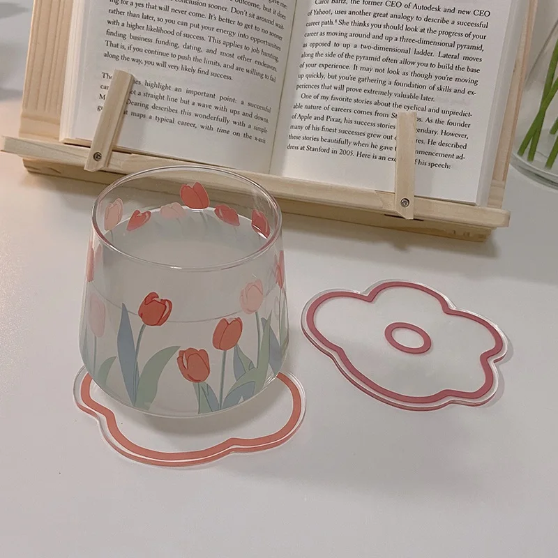 Un vaso con un diseño floral, concretamente tulipanes, colocado sobre una superficie. Al lado del vaso, hay un posavasos con un diseño floral similar, que parece ser un juego a juego.