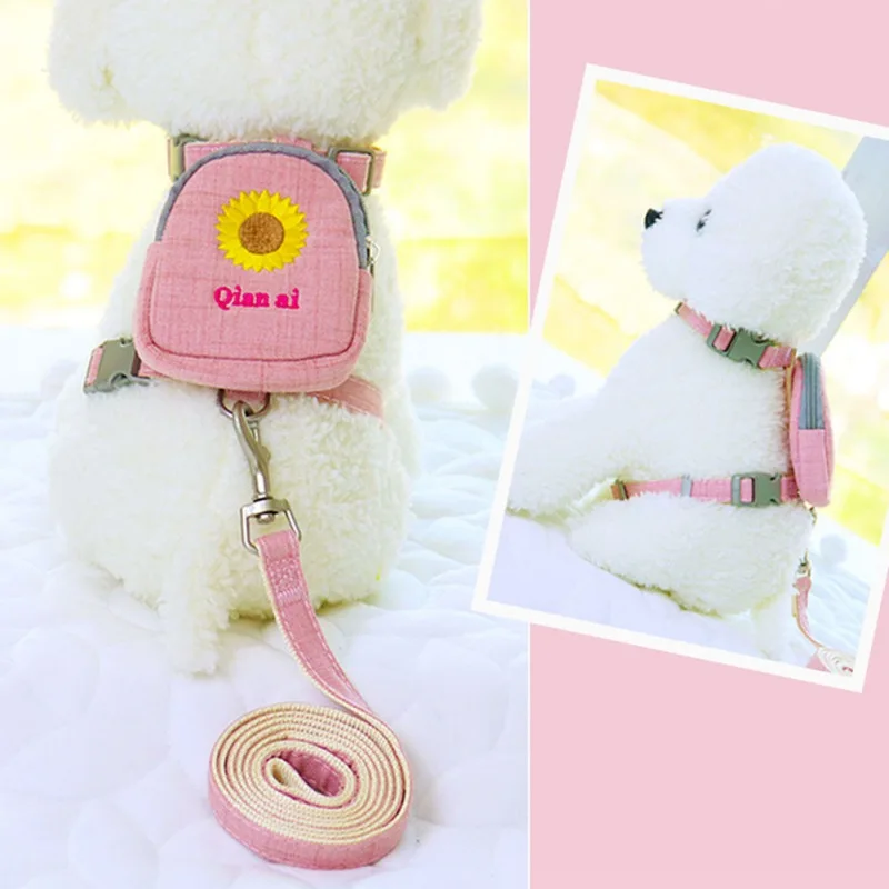 Un osito de peluche blanco que lleva una mochila rosa con un diseño de girasol. La mochila tiene una correa que está unida al cuello del oso, y hay una correa rosa unida a la mochila, lo que sugiere que el oso está diseñado para ser llevado o paseado como una mascota.