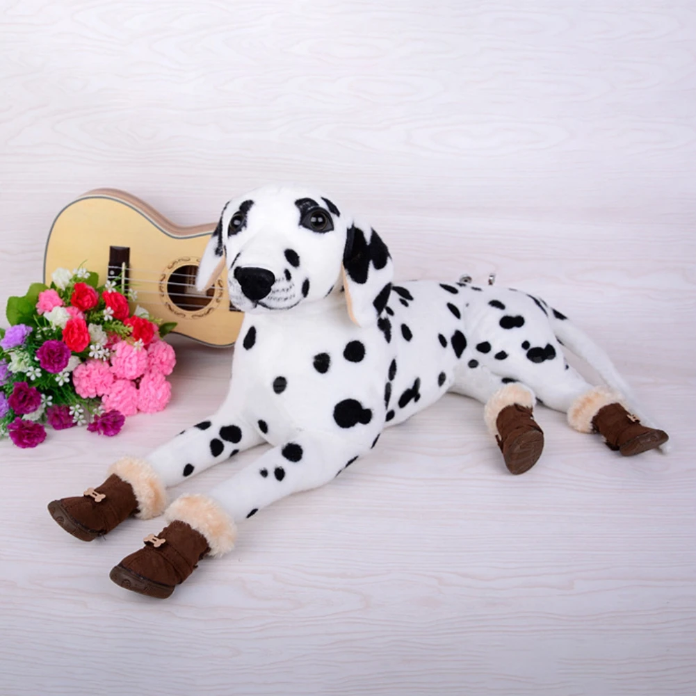 Un peluche que se parece a un perro dálmata. El juguete está tumbado de lado y lleva botas marrones con ribetes de piel. Al lado del juguete, hay una pequeña guitarra y un ramo de flores, que incluyen flores de color rosa y violeta.