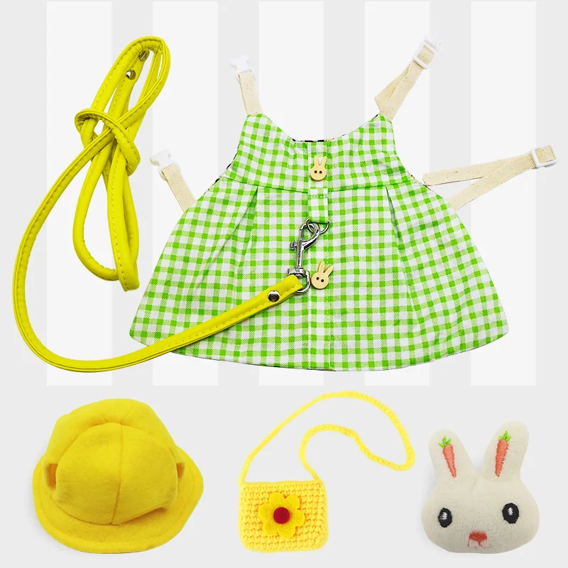 Una colección de artículos que parecen ser parte del atuendo o accesorios de un niño. Hay un vestido a cuadros verde y blanco con un cinturón amarillo y una hebilla amarilla. A la izquierda del vestido, hay una cuerda o correa amarilla, posiblemente para un bolso o un arnés.