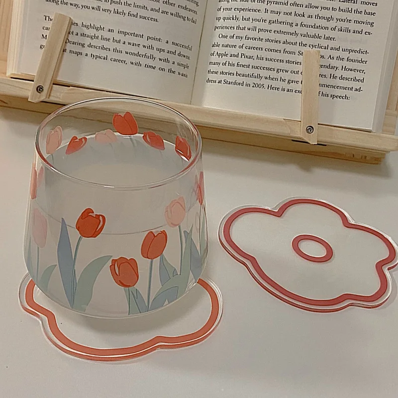 Un vaso con un diseño floral, concretamente tulipanes, colocado sobre una superficie. Al lado del vaso, hay un posavasos con un diseño floral similar, que parece ser un juego a juego.