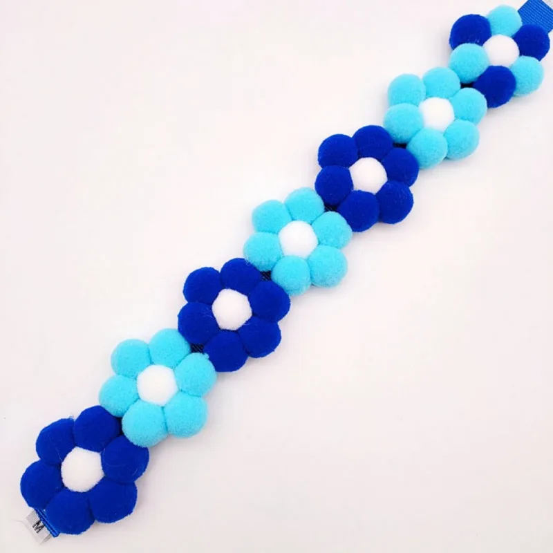 Pulsera de flores de fieltro azules y blancas. Las flores están dispuestas en un patrón y la pulsera parece estar diseñada para un niño o un adulto pequeño, dado su tamaño.