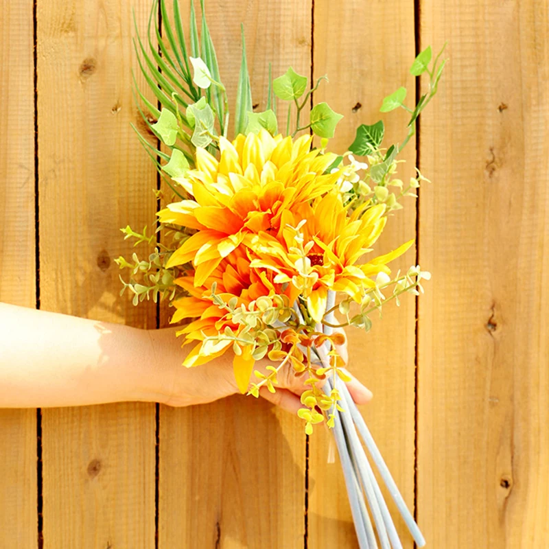 Un ramo de flores retenido sobre un fondo de madera. El ramo consta de flores de color amarillo brillante, posiblemente girasoles, y algo de vegetación, que podría ser aliento de bebé u otras flores pequeñas o follaje.