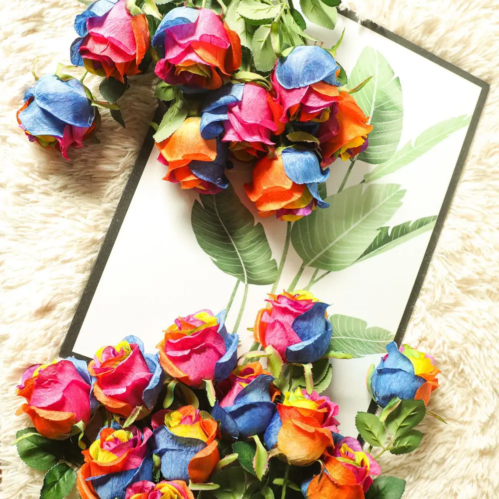 Un ramo de rosas de colores con varios tonos de rosa, azul, naranja y amarillo. Las rosas están dispuestas de forma que formen un corazón. El ramo se coloca sobre una superficie blanca con un borde negro, que podría ser un marco decorativo o un tapete.