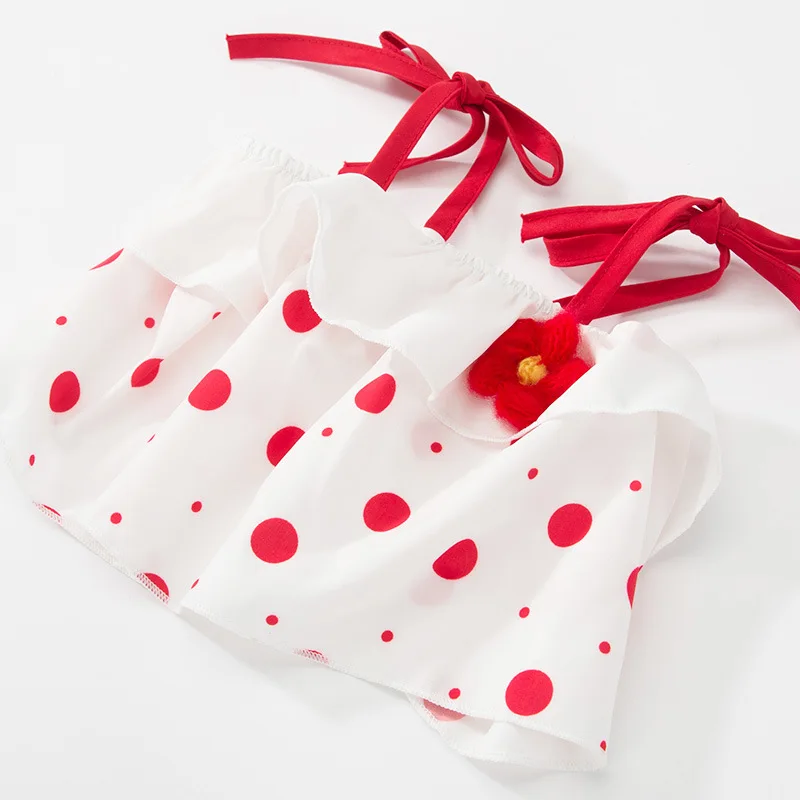 Una prenda de tela blanca con un estampado de lunares rojos. Parece ser una pieza decorativa, posiblemente un bolso o una tela decorativa, con una cinta roja atada a su alrededor. También hay una pequeña flor roja unida a la cinta, añadiendo un toque de adorno.