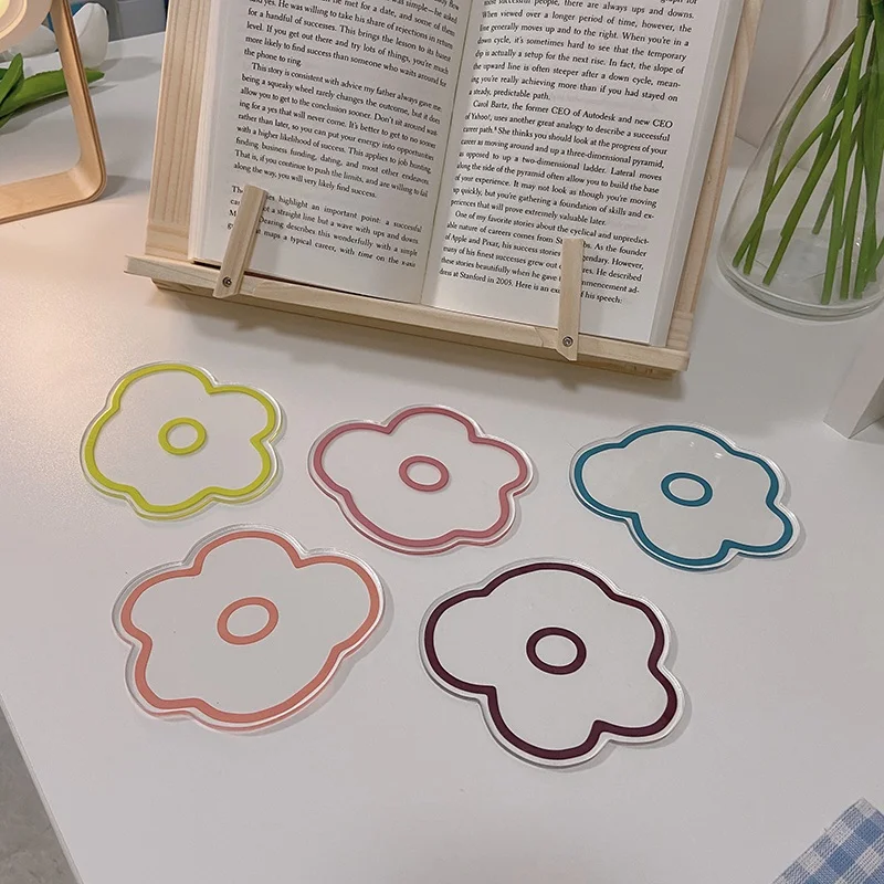 Un atril de madera con un libro abierto que muestra una página con texto. Delante del atril hay cuatro notas adhesivas o marcapáginas con forma de flor, cada una de un color diferente: amarillo, rosa, morado y azul.