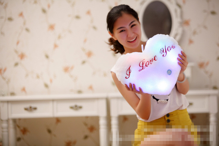 naeratav inimene hoiab südamekujulist LED padja, millel on kiri 'I Love You'