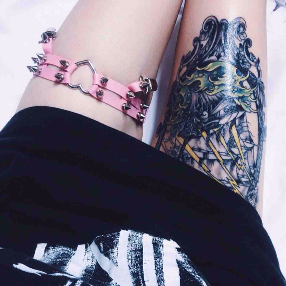 roosa sukahoidja metallist naastudega ja südamekujuline detail, kantud tätoveeritud jalal