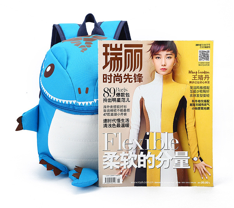 sinine dinosauruse kujuline seljakott laste jaoks, mille kõrval on ajakiri