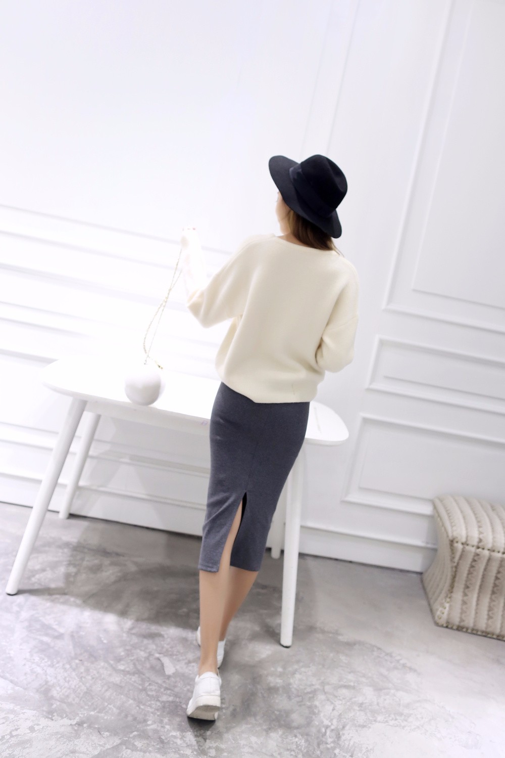 naine kannab halli pliiatsseelikut ja valget kampsunit, seistes valge laua juures