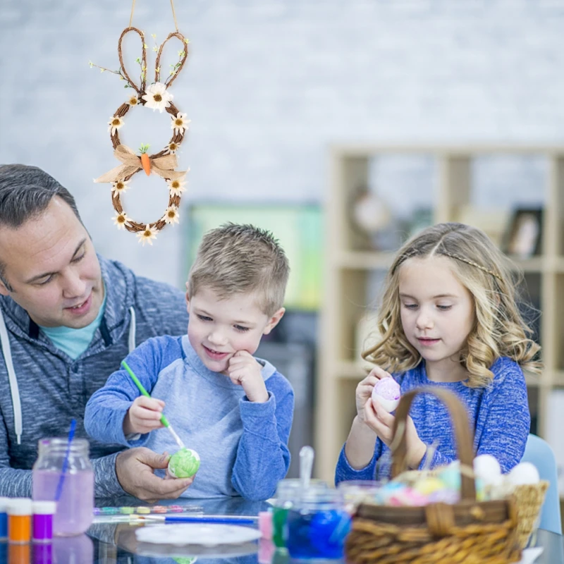 En la imagen aparece una familia de tres integrantes realizando una actividad que parece estar relacionada con la Semana Santa o la primavera. El hombre sostiene a un niño pequeño que sostiene un huevo verde, posiblemente de plástico, y parece que lo están decorando. El niño sonríe y mira el huevo.