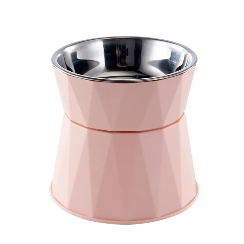 Un cuenco de agua para mascotas. Tiene un recipiente de acero inoxidable con una superficie reflectante, colocado dentro de un soporte de color rosa o coral que parece estar diseñado para mantener el recipiente elevado y estable. El soporte tiene un patrón geométrico y una base acampanada que proporciona estabilidad.