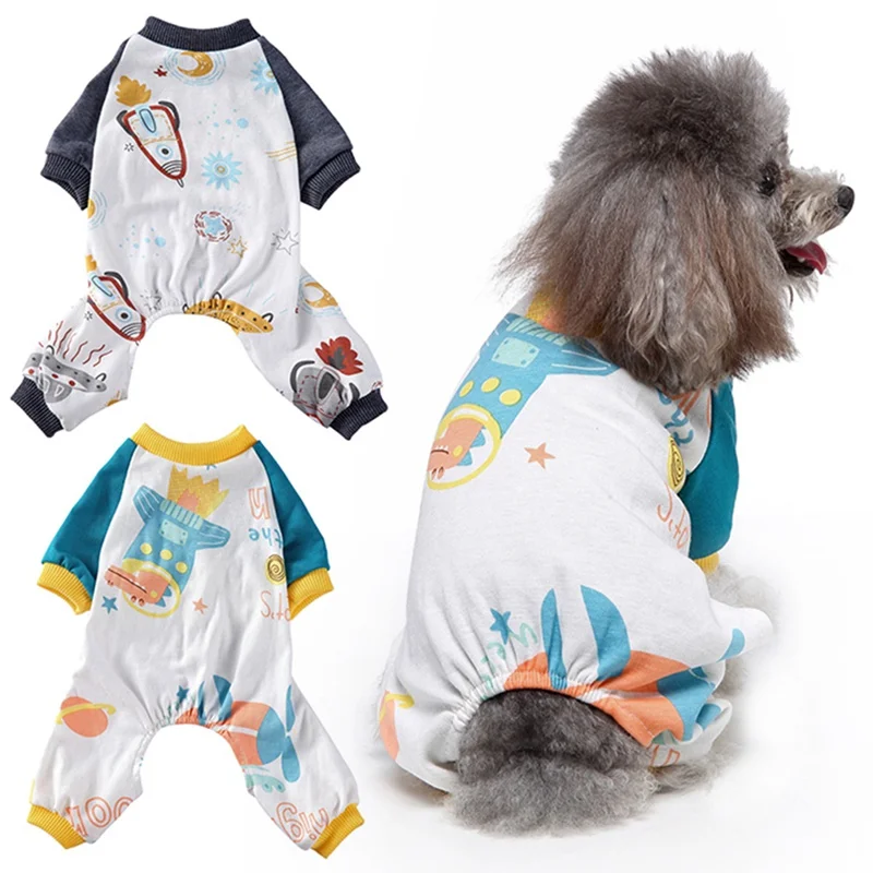 Un perro con un pijama de perrito. Los pijamas tienen un diseño divertido con varios patrones e imágenes coloridos, incluido lo que parece ser un cohete, un pez y otros elementos caprichosos.