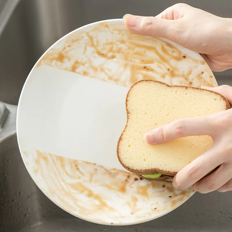 a person holding a toast shape dish washing sponge in front of a sink