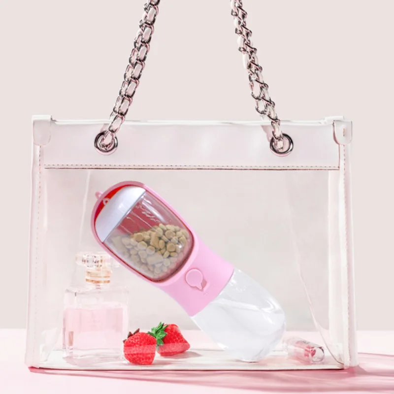 Un bolso transparente con interior rosa. Dentro del bolso hay una botella de agua rosa y blanca con un diseño en forma de corazón. La botella parece estar llena de un líquido marrón, posiblemente una bebida o un alimento líquido.