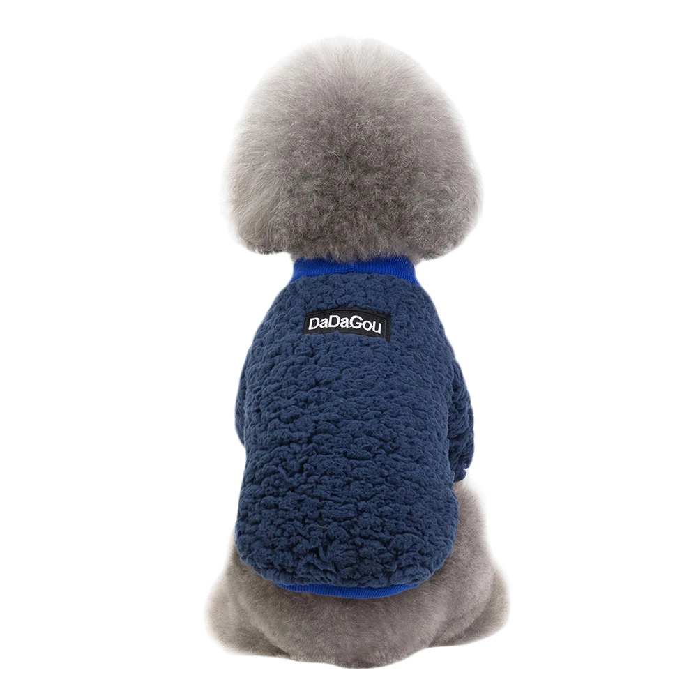 Un peluche que se parece a un perro. Tiene el cuerpo gris con textura esponjosa y cuello azul. El juguete está sentado erguido y parece estar diseñado para parecerse a un perro pequeño, posiblemente una raza con un pelaje parecido al de un caniche.