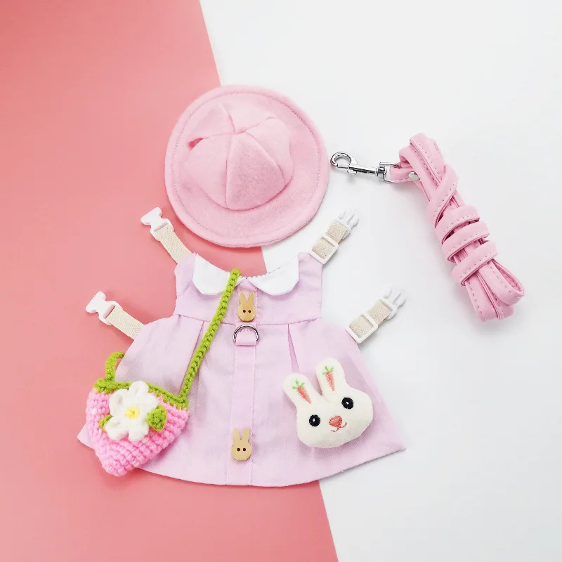 Una colección de artículos que parecen ser versiones en miniatura o de juguete de ropa y accesorios. Hay un vestido rosa con cuello blanco y un motivo de conejito en la parte delantera, un sombrero rosa con un lazo, un bolso rosa con una flor blanca y una correa rosa con un clip.