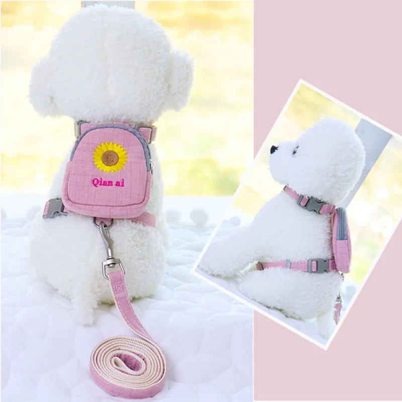 Un osito de peluche blanco que lleva una mochila rosa con un diseño de girasol amarillo. La mochila tiene una correa que pasa por encima del hombro del oso y una correa rosa adjunta.