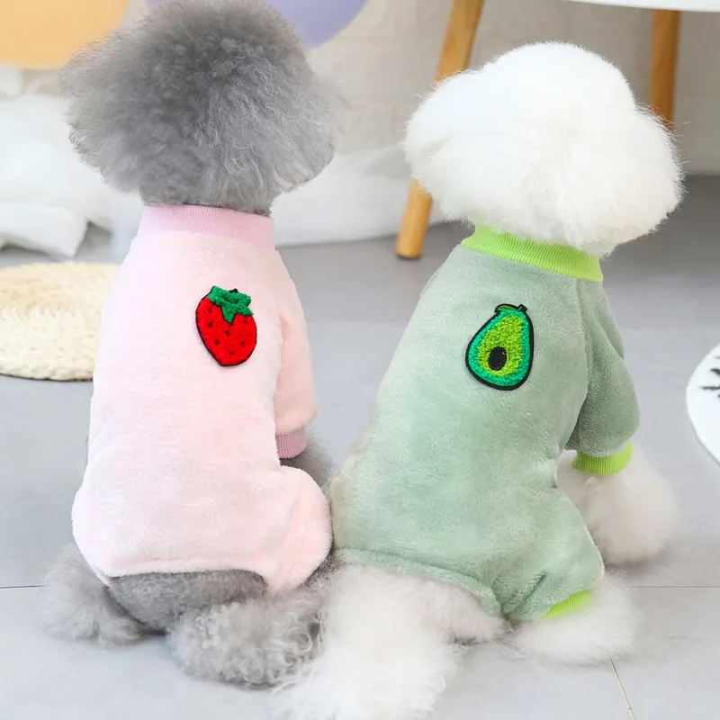 Dos peluches que parecen perros. Llevan trajes a juego con un diseño de fresa y aguacate en la espalda, lo que sugiere un tema de alimentación saludable o un juego con la idea de las golosinas para perros.