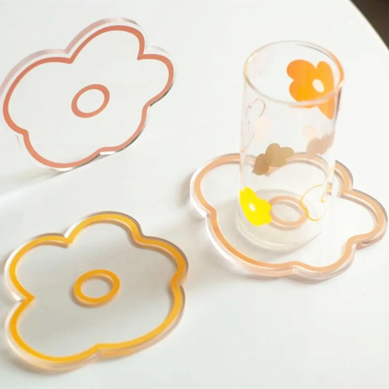 Un vaso transparente con diseño floral, colocado sobre una superficie blanca. Alrededor del cristal hay tres objetos con forma de flores que, dada su forma y disposición, parecen elementos decorativos o posiblemente cortadores de galletas.