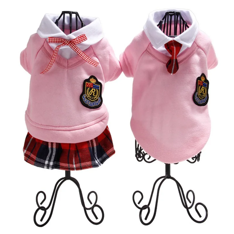 Dos maniquíes vestidos con un traje estilo uniforme escolar. El conjunto consta de una blusa rosa con cuello blanco, una falda a cuadros roja y azul y una corbata roja. La blusa tiene una insignia o emblema en el lado izquierdo del pecho.