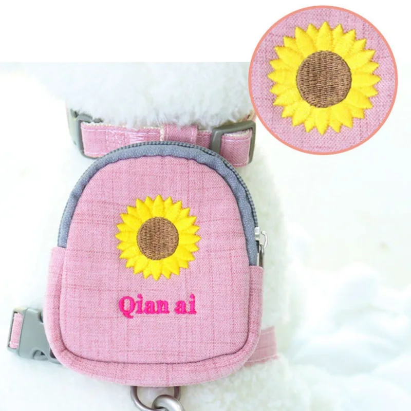 Una mochila rosa con un diseño de girasol. La mochila tiene una correa gris y un panel gris en la parte delantera. Hay una etiqueta con el nombre en el frente de la mochila que dice Qian ai, que podría ser un nombre o una marca.