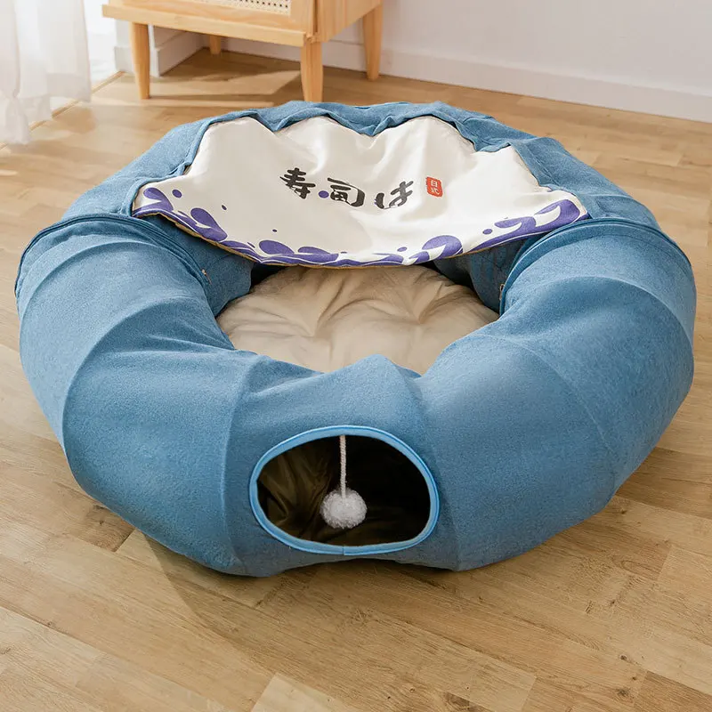 Una cama para mascotas diseñada para gatos. Tiene forma circular con borde elevado y interior acolchado. Hay un área pequeña y cerrada en un lado, que probablemente esté destinada a que el gato se acurruque para mayor comodidad y seguridad.