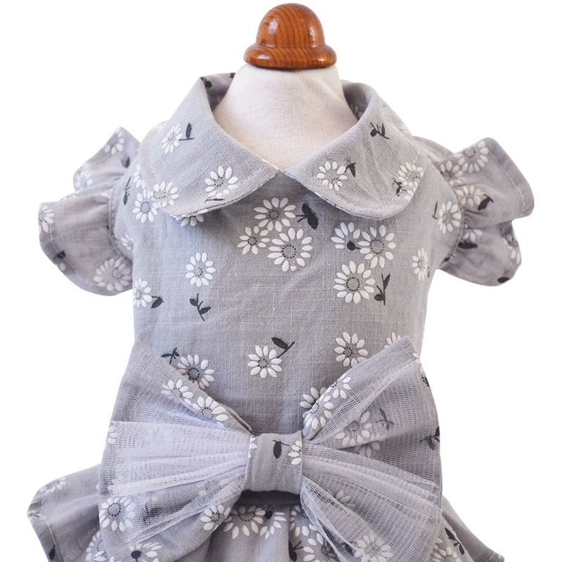 Un maniquí vestido con un vestido de niño. El vestido tiene un estampado floral con flores blancas y contornos negros, y presenta un lazo en la cintura. El maniquí tiene una cabeza de madera y está diseñado para exhibir ropa.