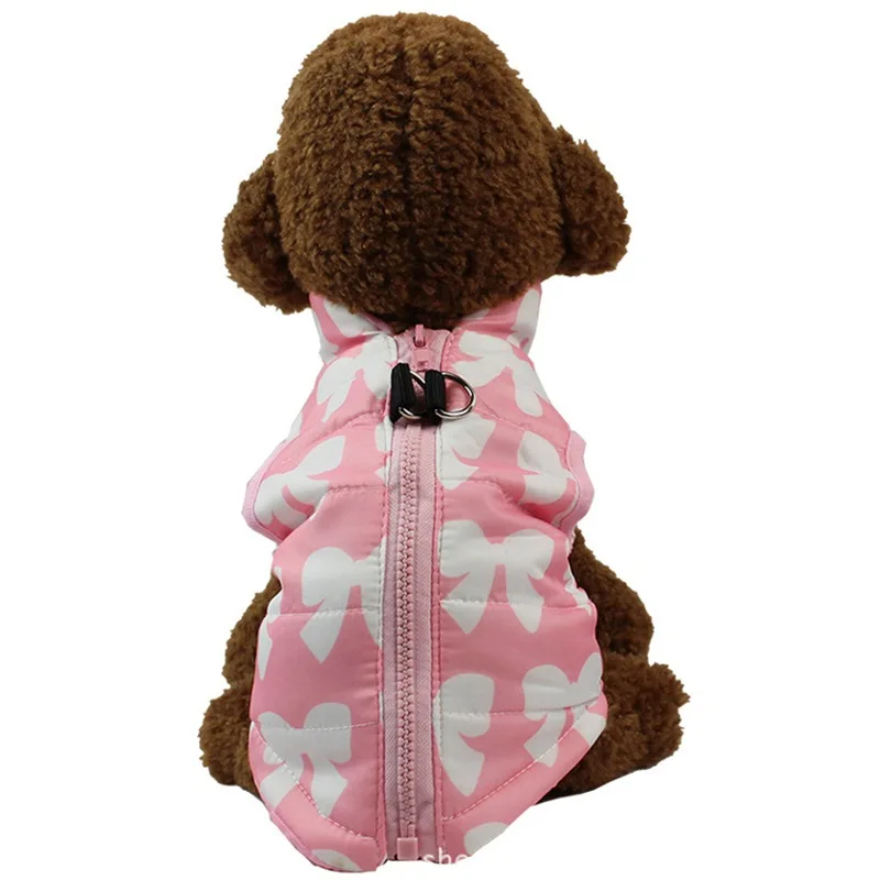 Un osito de peluche marrón que lleva una chaqueta rosa y blanca con un diseño de lazo. La chaqueta tiene una cremallera en la parte delantera y un pequeño botón negro en la espalda. El oso parece estar sentado y la chaqueta está diseñada para ajustarse cómodamente a su cuerpo.