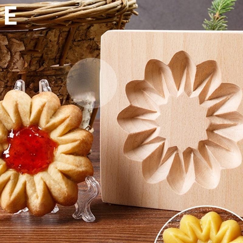 A cookie featuring a flower shape with a red jam center is elegantly displayed on a small stand, paired with the Wooden 3D Cookie Cutters, Christmas Biscuit Cutter which highlights its carved patterns in beech wood. In the background, a woven basket and green foliage add to the scene.