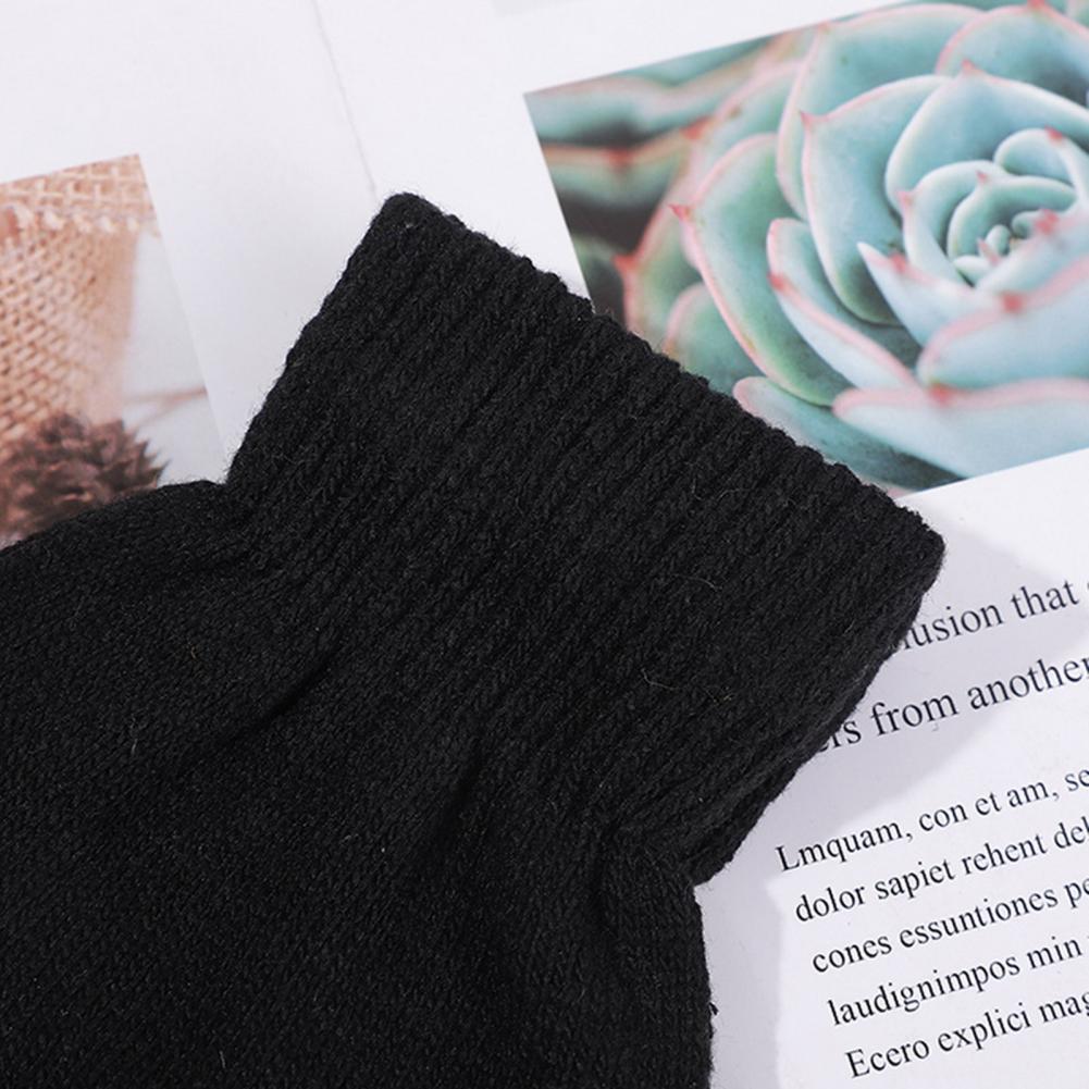 Lähivõte mustadest kudumitest, mis kuuluvad laste Soodsad sõrmikud lastele komplekti, asetatud valge paberi ja rohelise taime pildi taustale.