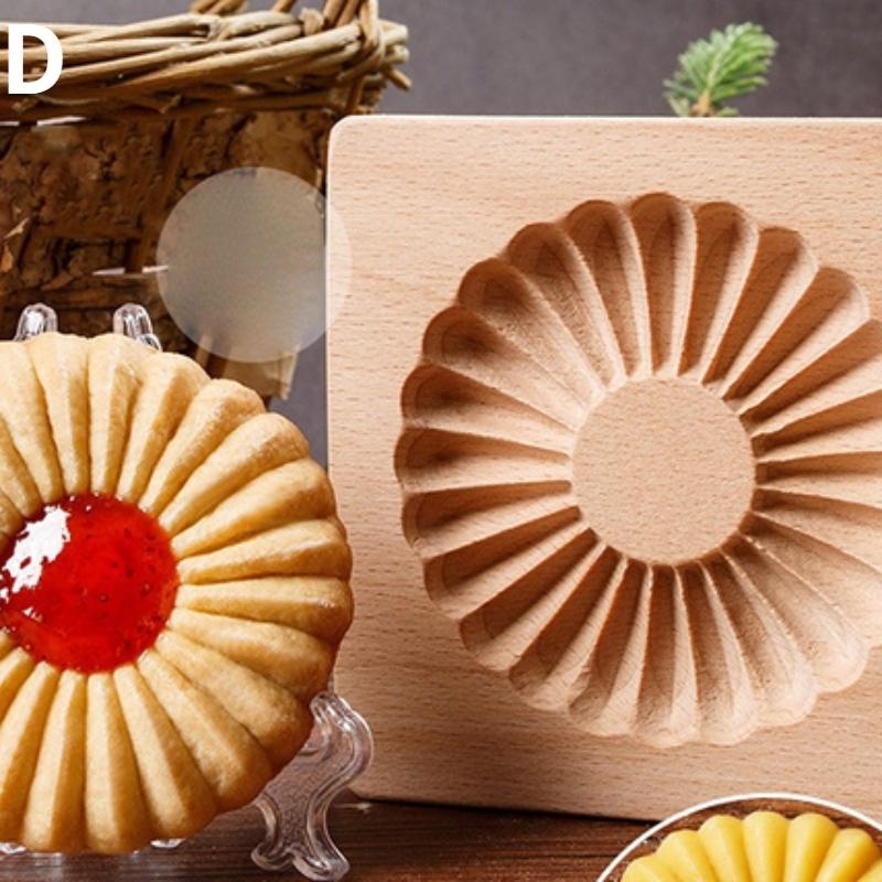 A detailed wooden embossing mold, specifically the "Wooden 3D Cookie Cutters, Christmas Biscuit Cutter," featuring carved patterns, is displayed next to a sunflower-shaped cookie with a red jam center. Both the mold and cookie are set on a table, with a woven basket and small plant in the background.