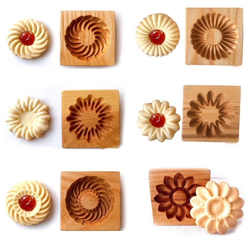 Wooden 3D cookie cutters and matching cookies are on display. The molds feature intricate carved floral patterns, and the corresponding cookies placed above boast similar floral designs with jam centers.