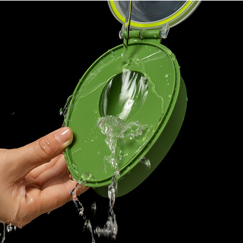 A hand holds the Avocado Crisper Box Airtight, allowing water to be poured onto the green, oval-shaped container. Water cascades through the middle opening and overflows against a black background.